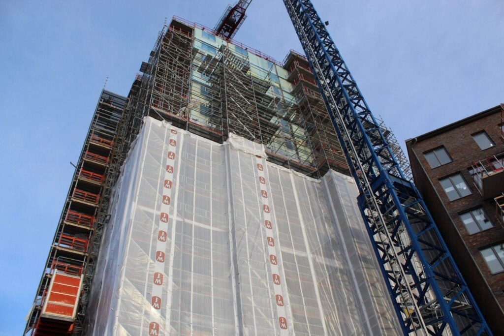 Profiled scaffolding fabric, also called scaffolding plastic with M logo clad on scaffolding at the building site in Bolinder Strand.